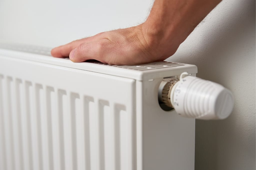 Käsi patterin päällä, vieressä termostaatti numeroasteikkoineen