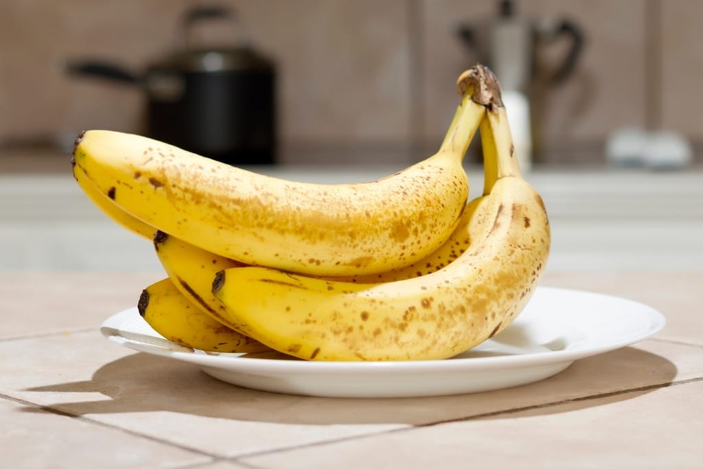 Ruskeapilkkuisia kypsiä banaaneja valkoisella lautasella keittiön pöydällä.