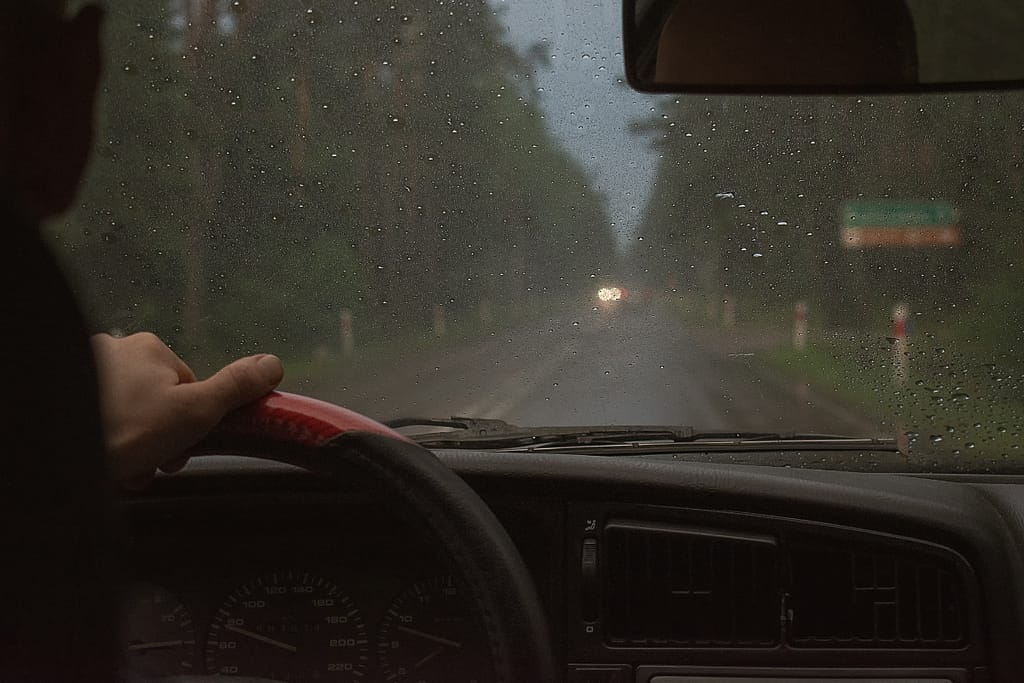 Henkilö ajaa autoa pimeällä ja sateisella säällä.