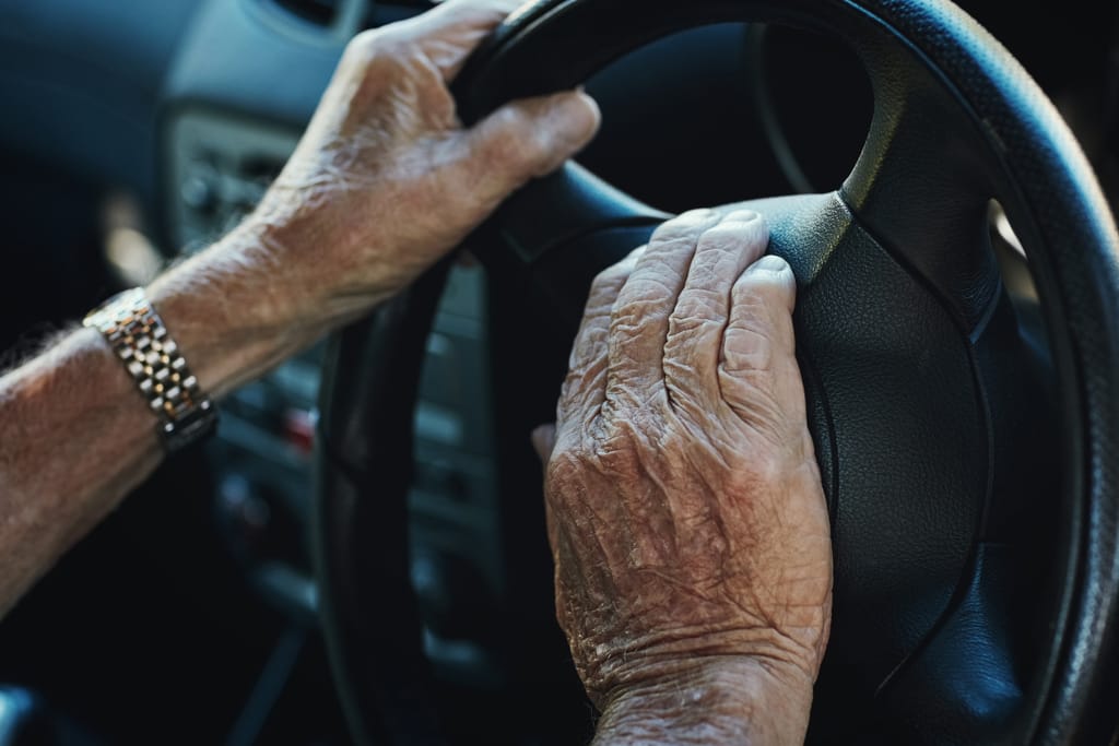 Seniorin kädet auton ratissa.