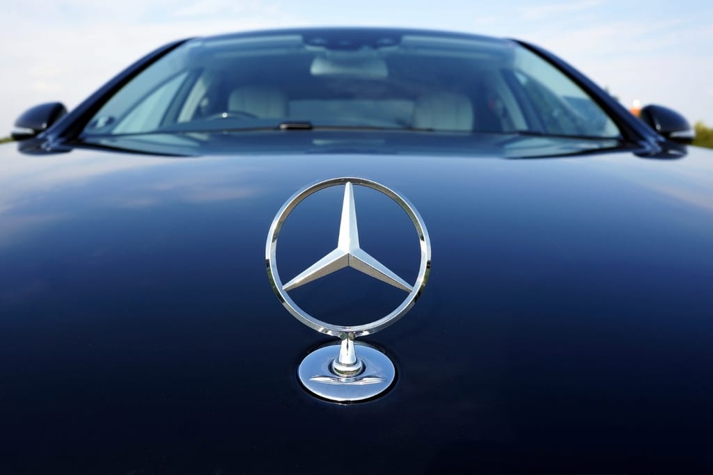 Hopeinen Mercedes-Benzin tähtitunnus tummansinisen henkilöauton konepellillä, auton tuulilasi taustalla.