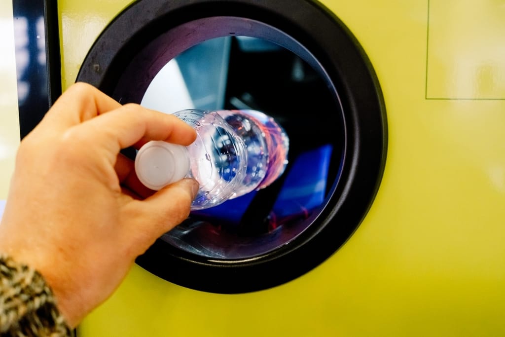 Käsi palauttaa tyhjää muovipulloa keltaiseen pullonpalautusautomaattiin.
