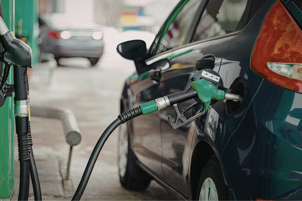 Tumma henkilöauto tankattavana huoltoasemalla. Vihreä polttoainepistooli on kiinnitetty auton tankkausaukkoon.