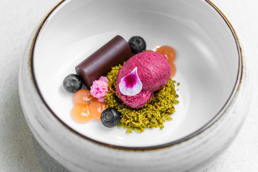 Moderni jälkiruoka-annos: marjajäätelöä, suklaaelementti ja hedelmäisiä lisukkeita valkoisella lautasella.
