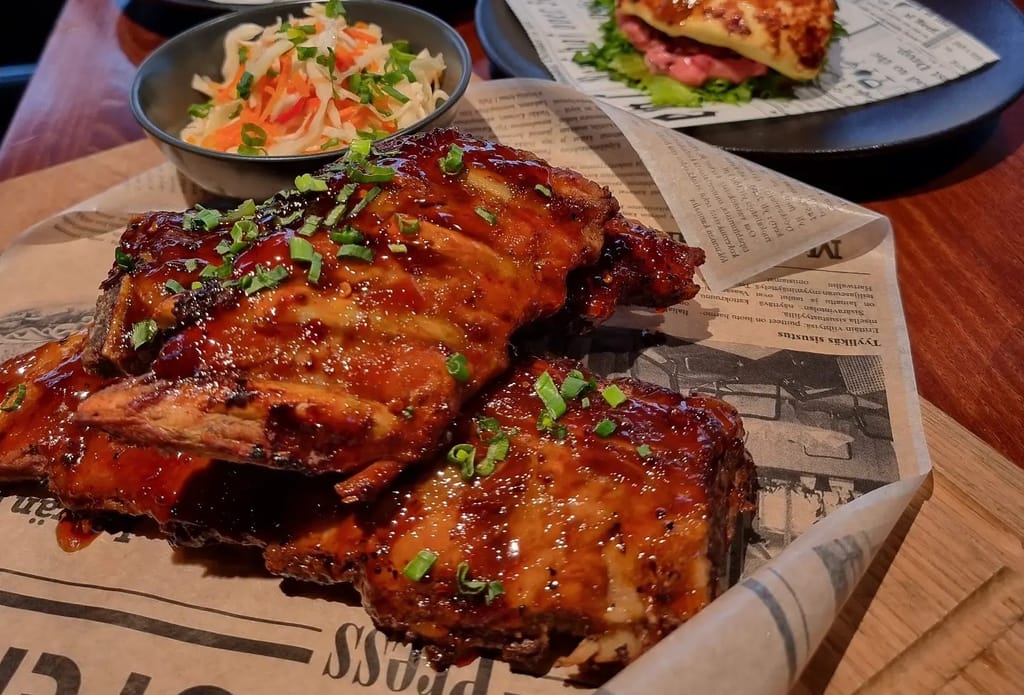 Glaseerattuja ribsejä paperin päällä, päällä kevätsipulia, vieressä kaalisalaattia.