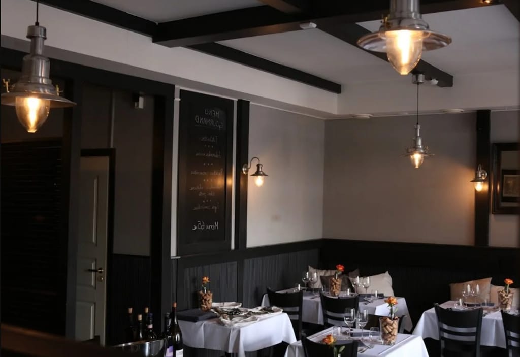 "Ravintolan sisätila, jossa katetut pöydät, valkoiset pöytäliinat ja hillitty valaistus.