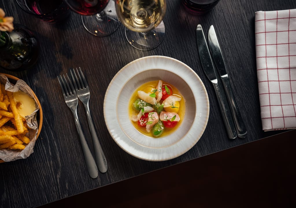 Birdie Numnumin annos pöydällä. Lautasella tomaatteja ja raakaa kalaa viinilasillisen kera.