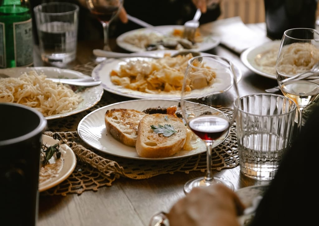 Ravintolapöytä, jossa useita pastaruokia, paahdettua leipää ja viinilaseja yhteisellä aterialla.