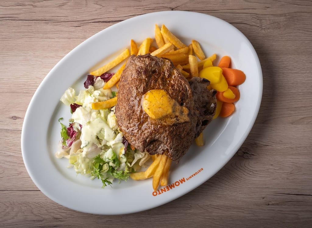 Pihvi ranskanperunoilla, vihersalaatilla ja keitetyillä kasviksilla valkoisella lautasella.