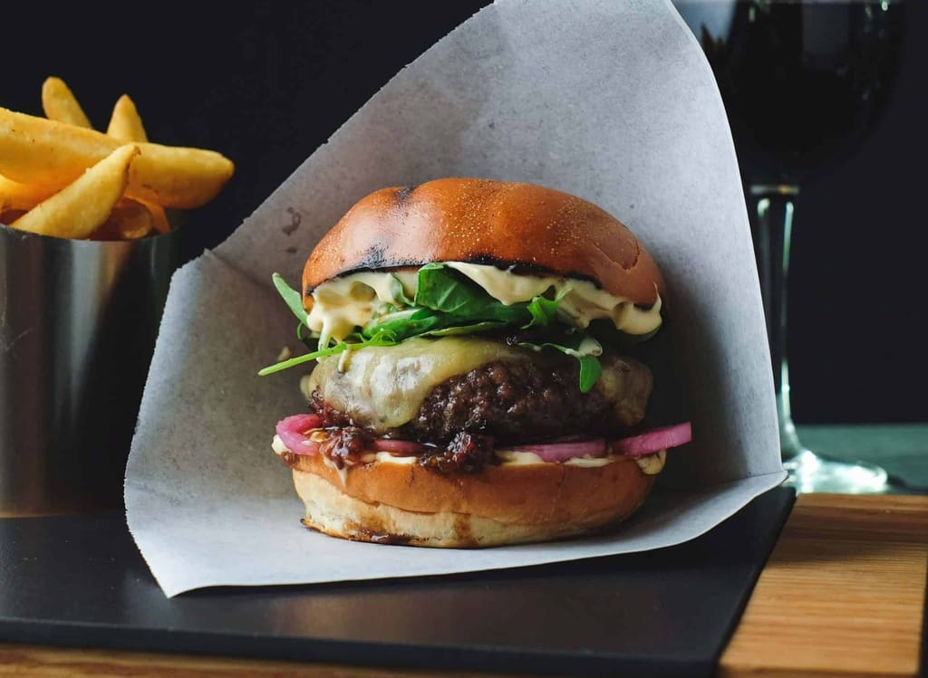 Paperin sisässä hampurilainen, jonka välissä pihviä, juustoa ja salaattia. 