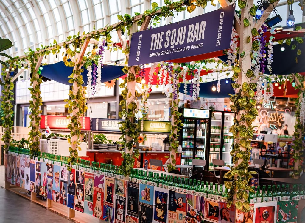 Korealainen The Soju Bar -ruokakoju sisähallissa, vihreillä kasveilla ja sojupulloilla koristeltuna.