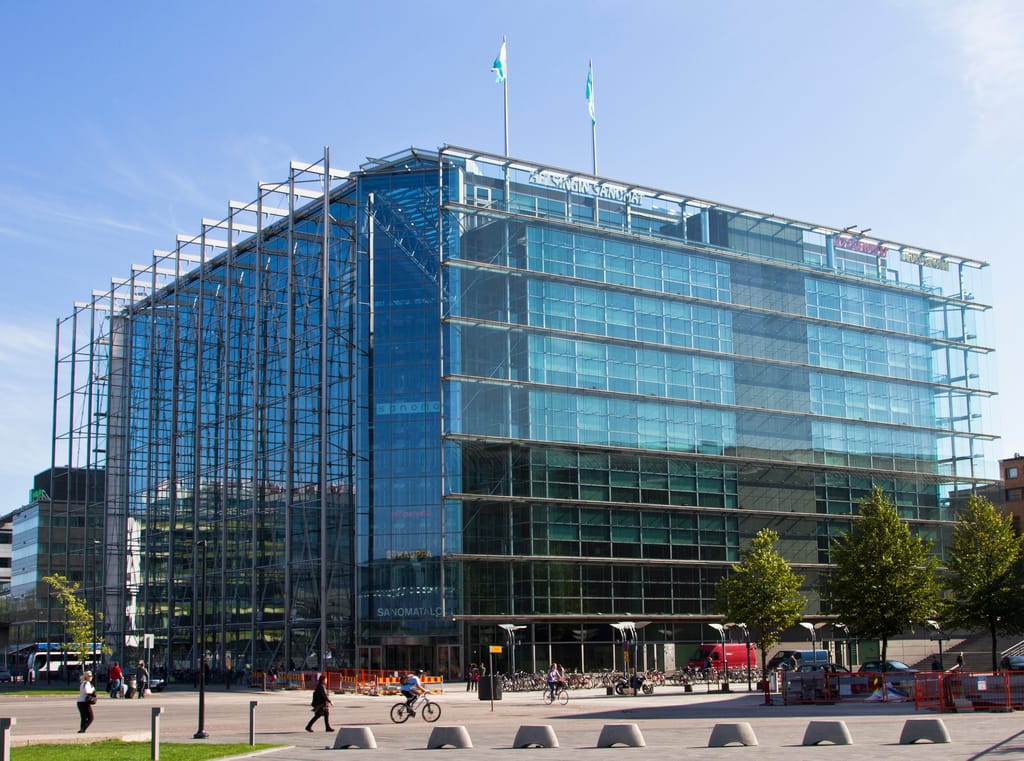 Helsingin Sanomatalo päivänvalossa – moderni lasiseinäinen rakennus, jonka katolla liput liehuvat.