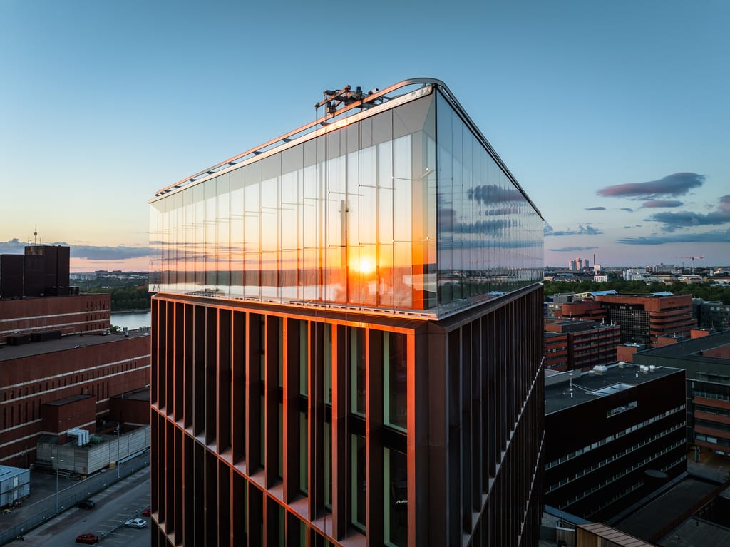 "Moderni lasinen toimistorakennus kaupunkimaisemassa auringonlaskun aikaan.