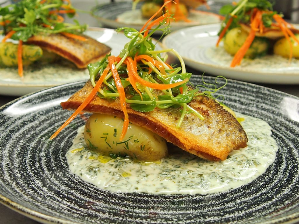 Ravintola Karl Johanin paistettu kala-annos, perunaa ja yrttikastiketta lautasella.