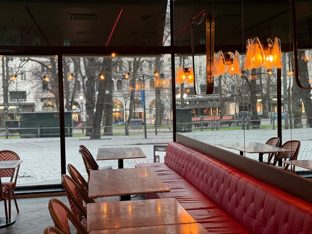 Ravintolasalin ikkunapöytiä ja punaisia nahkasohvia, taustalla kaupunkinäkymä ja lämmin tunnelmavalaistus.
