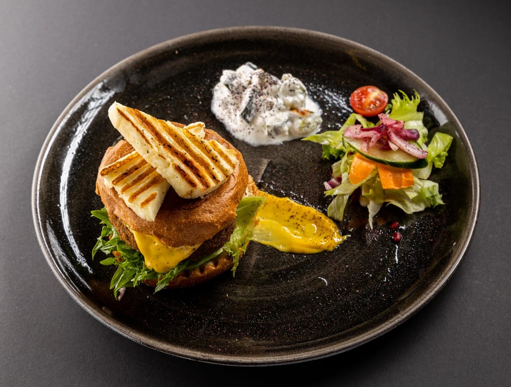 Kasvisburgeri grillatulla halloumilla, lisukkeena salaatti ja kastikkeita.