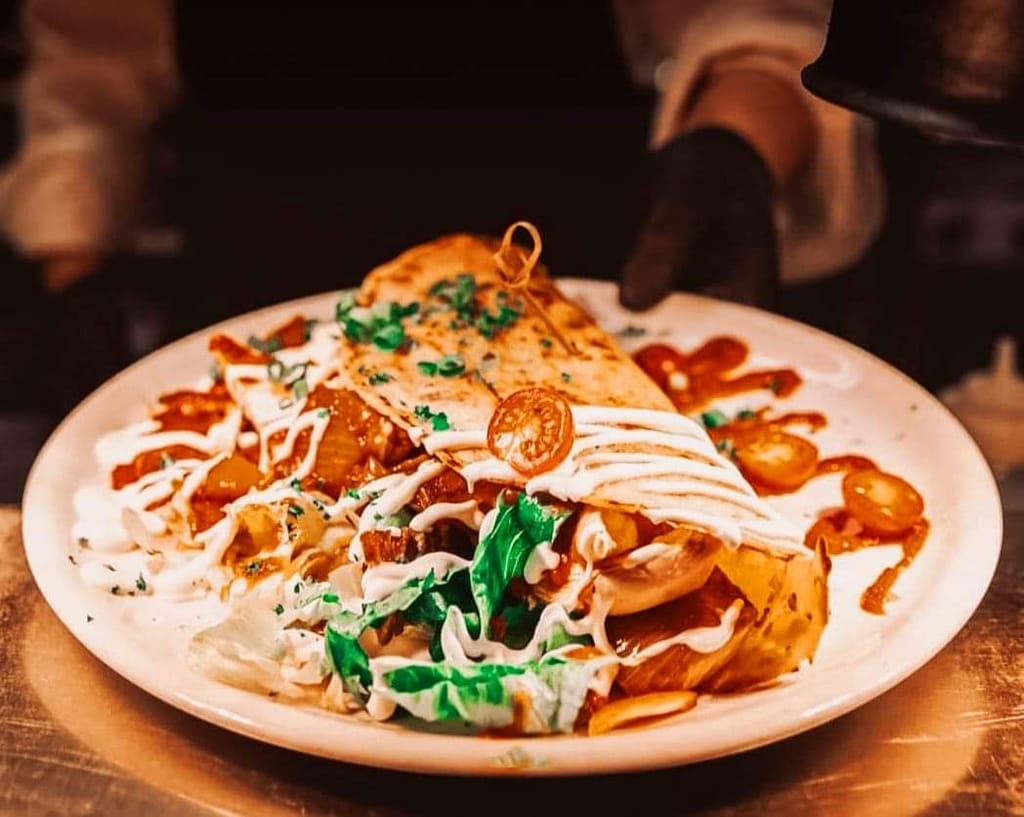 Suuri täytetty tortilla-annos, jossa lihaa, vihanneksia ja valkoista kastiketta, tarjoiltuna lautasella ravintolassa.