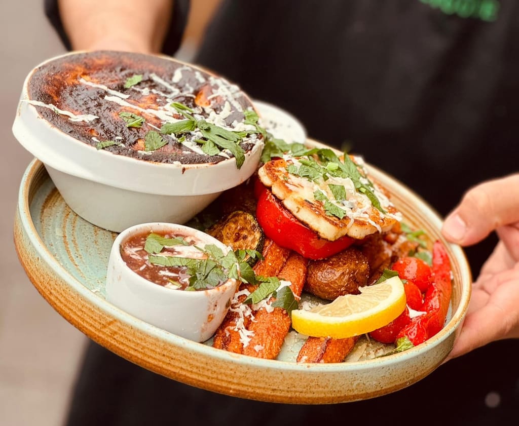 Tarjoiltu kasvisannos, jossa grillattua juustoa, paahdettuja perunoita, paprikaa ja kastikkeita.