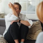 Nainen itkee terapeutille ja istuu vastapäätä sohvalla, pyyhkii nenäänsä