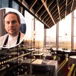 Ravintolasali suurine ikkunoineen ja viinikaappeineen, etualalla kokin muotokuva.