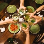 Ihmiset kohottavat laseja pöydän ääressä ja kilistävät vihreitä juomia yhteisen hetken kunniaksi.