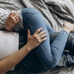 Kaksi aikuista makaa sängyssä kyljellään, toisen käsi lepää toisen reidellä