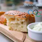 Laudalla pala focaccia-leipää. Vieressä tuorejuustoa kupissa ja kuvan päällä olympialaisten logo.
