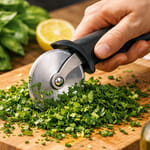 Pizzaleikkuri pilkkoo tuoreita yrttejä leikkuulaudalla keittiössä, ympärillä basilikaa, sitruuna ja oliiviöljypullo.