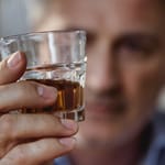 Mies pitelee kädessään lasillista ruskeaa alkoholia ja katsoo sitä vakavana.