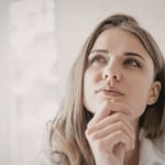 Nuori nainen katsoo ylös mietteliäänä ja pohtii ajatuksiaan valoisassa sisätilassa