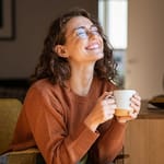 yksin viihtyvä nainen nauttii kahvista kotona hymyillen