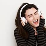 Nainen kuuntelee musiikkia kuulokkeilla silmät kiinni ja eläytyy voimakkaasti