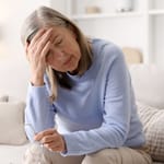Väsynyt nainen pitelee päätään sohvalla – jatkuva uupumus voi liittyä matalaan ferritiiniin