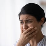 Nainen kokee pahoinvointia ja stressiä, käsi suun edessä