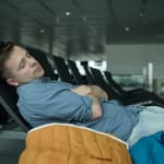 Mies nukkuu lentokentän penkillä vieressä takki.