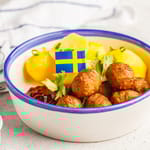 Kulhollinen lihapullia, perunoita ja puolukkahilloa, annoksessa pieni Ruotsin lippu.