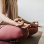 Henkilö meditoi rauhallisesti istuen lattialla käsi mudrassa