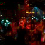 Ihmisiä tanssimassa vilkkaalla yökerhon tanssilattialla värikkäiden valojen loisteessa.