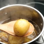 Puulusikalla nostettu keitetty peruna höyryävästä kattilasta liedellä.