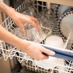 Kädet asettavat laseja ja astioita astianpesukoneen koriin.