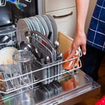 Henkilö täyttää astianpesukonetta laittamalla astioita ja ruokailuvälineitä sisään.