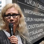 Anneli Auer puhuu mikrofoniin Turun oikeustalon edessä Varsinais-Suomen käräjäoikeuden kyltin vieressä.