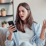 nainen turhautuneena selaa deittisovellusta puhelimella kotona