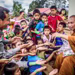 Munkki jakaa ruokaa lapsille ja perheille Aasiassa – hyväntekeväisyys ja avun tarve korostuvat globaalissa eriarvoisuudessa