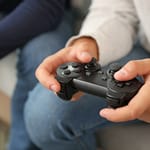 Mies istuu sohvalla ja pelaa pelikonsolilla.