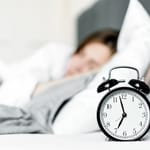 Herätyskello etualalla, nainen nukkuu taustalla