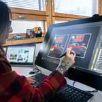 Graafinen suunnittelija työskentelee tietokoneella toimistossa luovassa työssä.