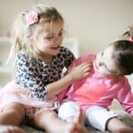 Kaksi tyttölasta leikkii kotona lattialla.