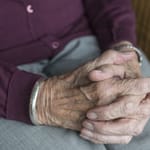 Vanhan naisen kädet ristissä polvien päällä.