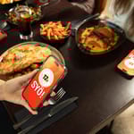 Ravintolapöydässä selataan puhelimista SYÖ!-viikkojen sivua. Taustalla annoksia.